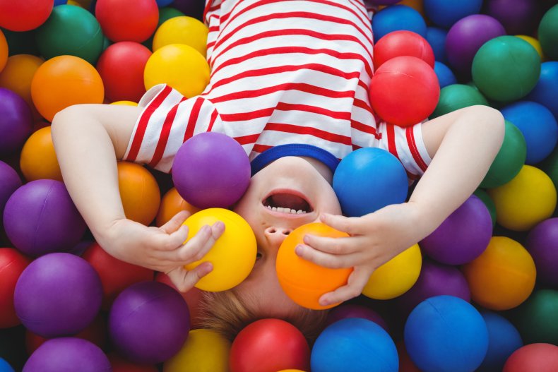 Cute smiling boy in sponge ball pool covering eyes with balls