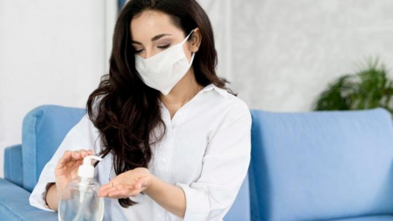 Woman sanitizing hands and wearing a mask