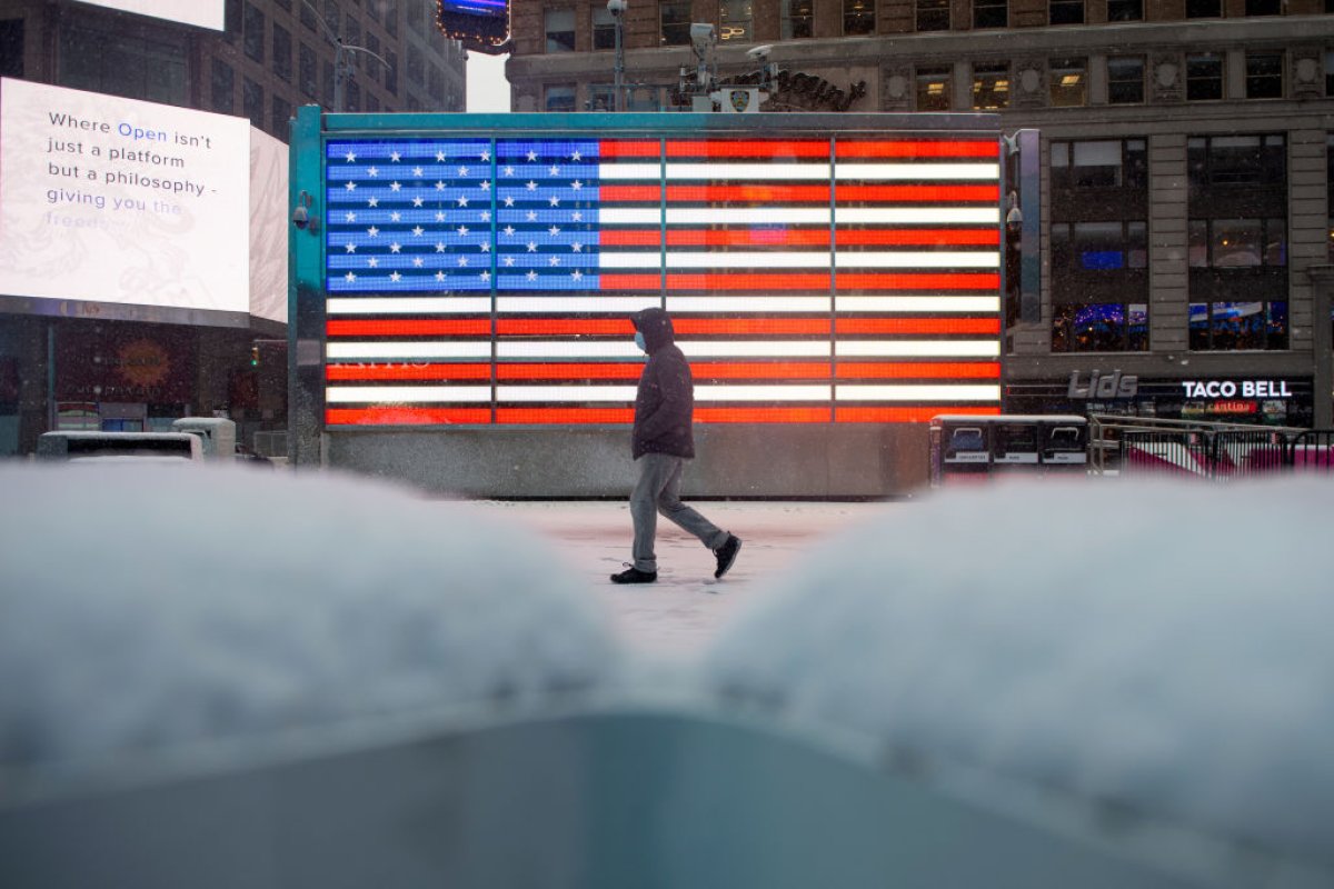 Person in facemask walks past American flag