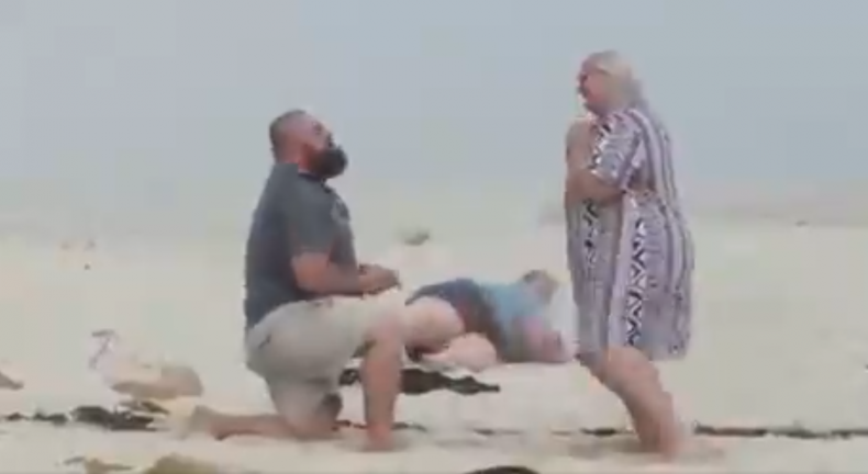 Man proposing on beach as photographer falls.