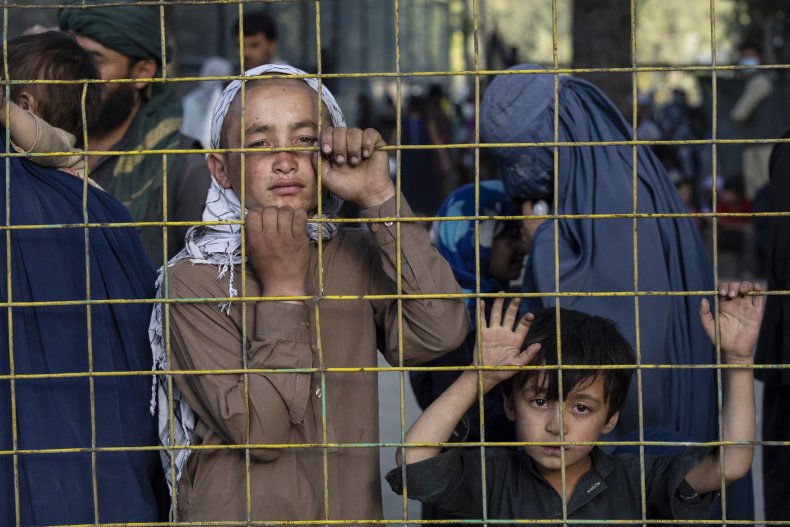 Displaced Afghans look through a fence