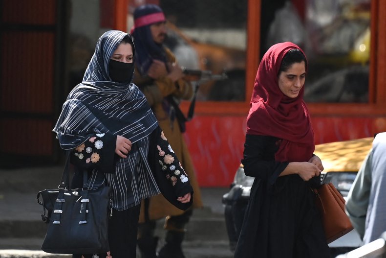 Afghan women walk past a Taliban fighter