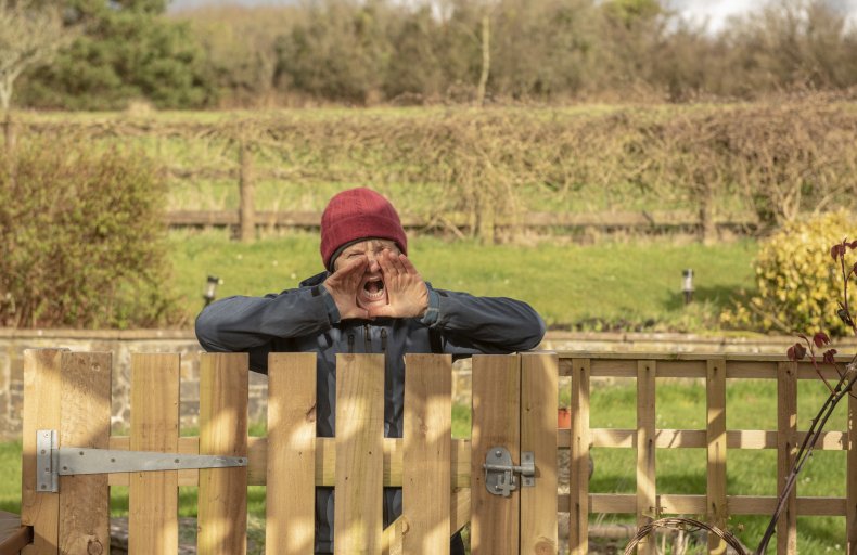 An elderly woman shouting over a fence.