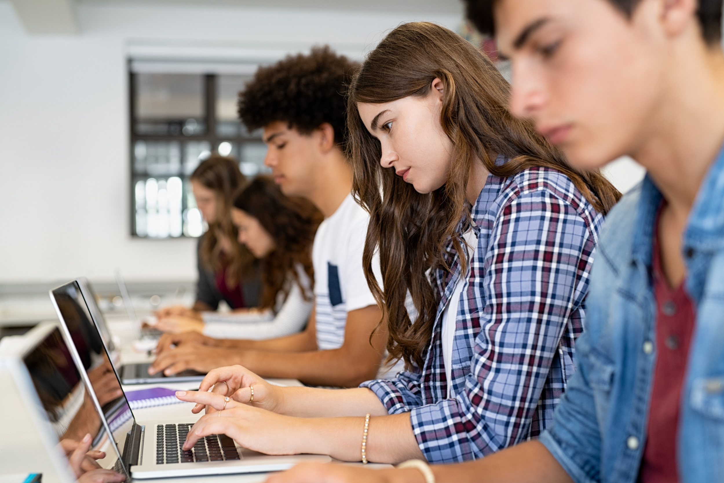  Students sitting in a row and using laptop computers in a classroom.