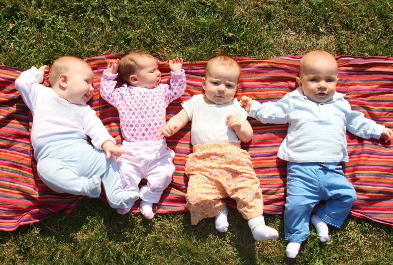 Four babies lying on blanket on grass
