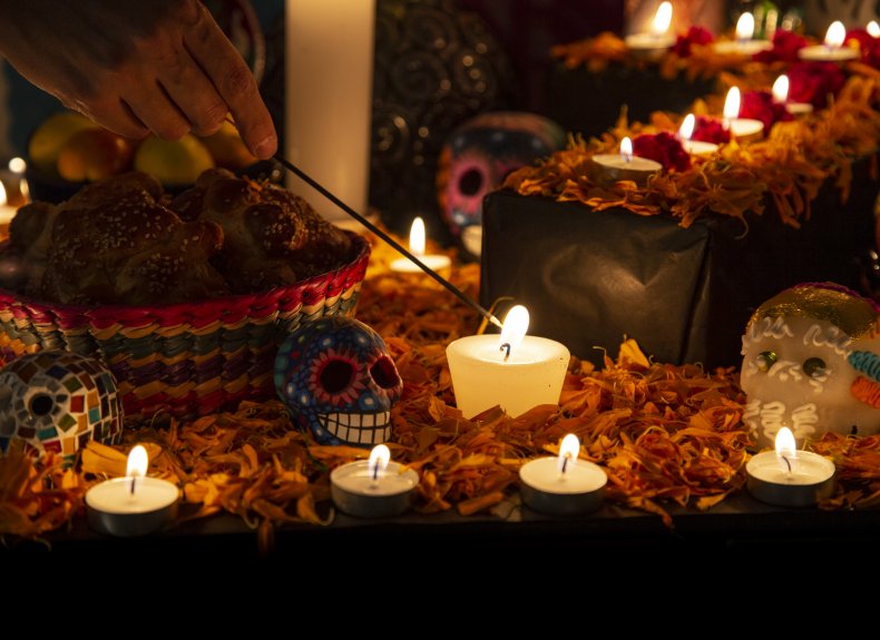 Woman lights a candle on an ofrenda.