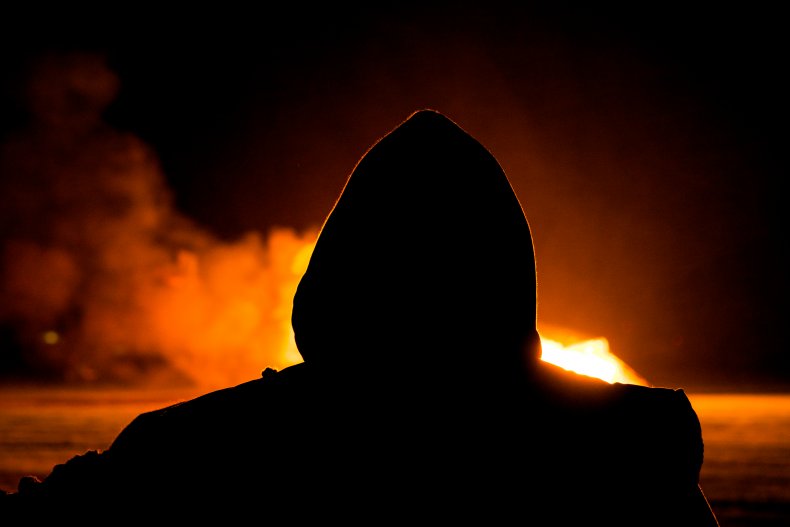 A hooded man looking at fire