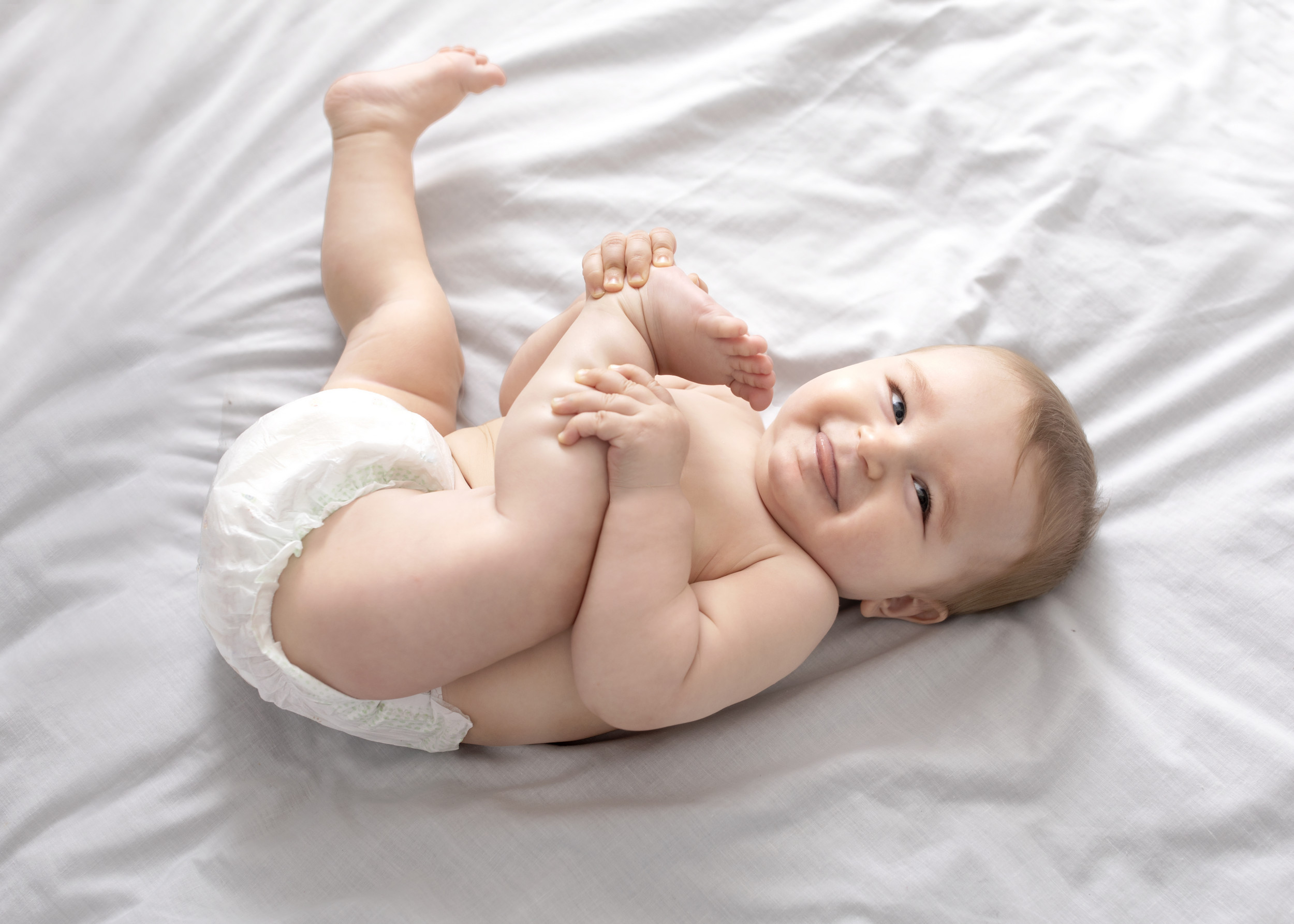 Малыш в памперсе лежащий на кровати играющий ногами