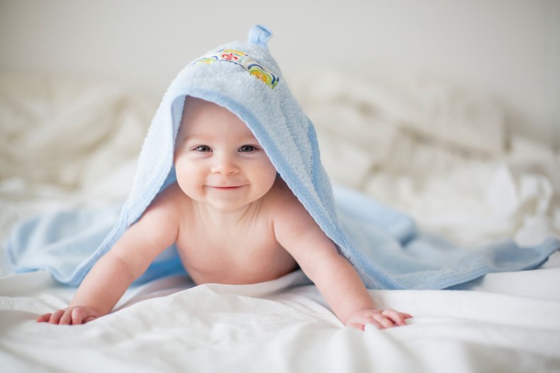 A smiling baby wearing cape towel.