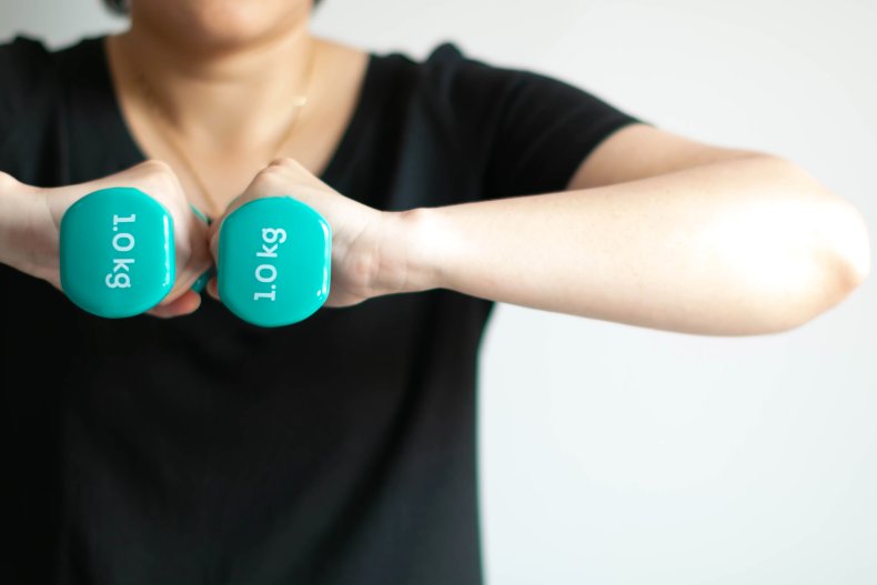 A woman holding up two dumbells.