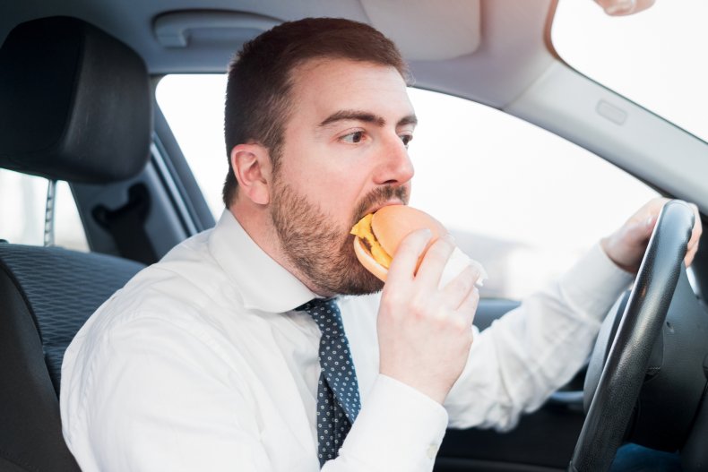 Man eating a burger in his car.