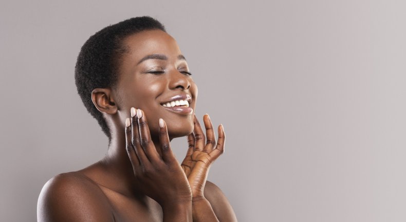 A smiling woman touching her face.