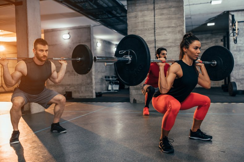 People doing a squat with barbell.