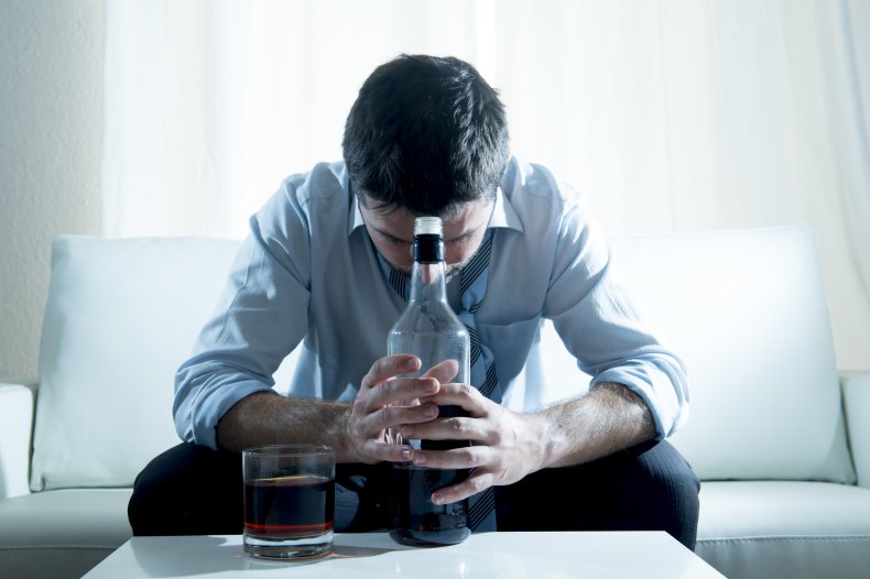 A man hunched over bottle of alcohol.