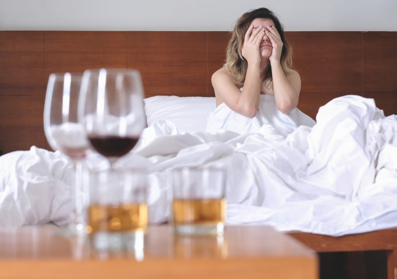 A woman in bed, with alcohol nearby.