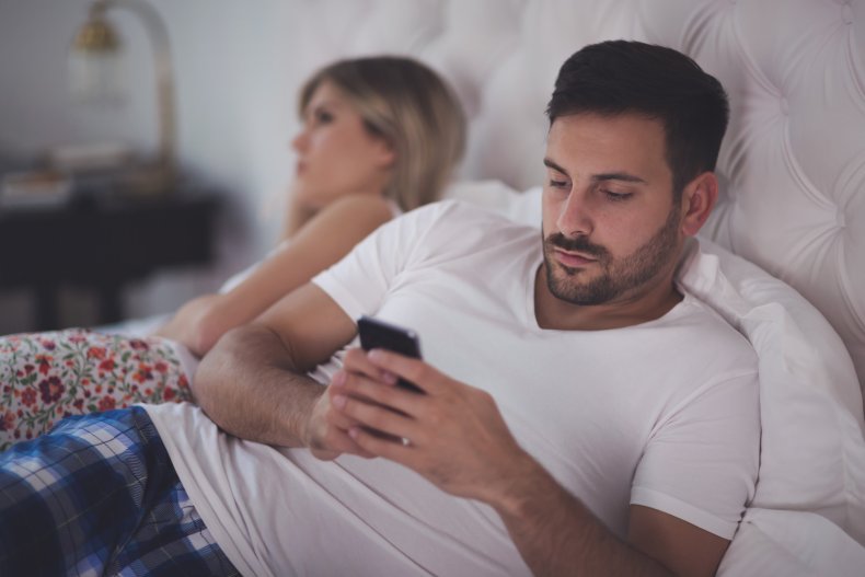 A couple in bed, man using phone.