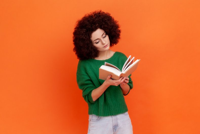 A woman reading book near orange wall.