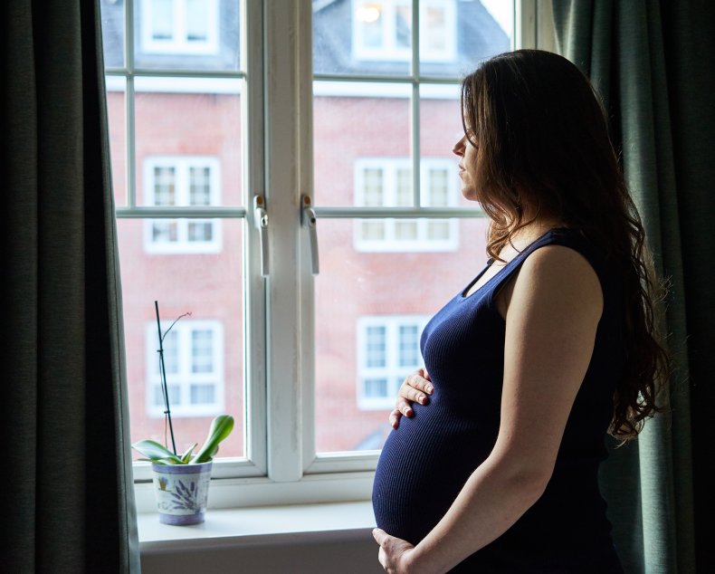 Pregnant woman staring out of window sadly