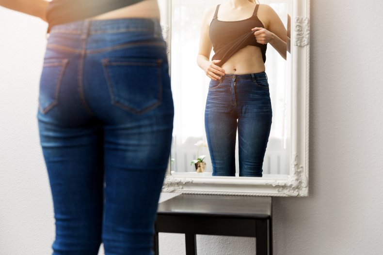 A woman looking at stomach in mirror. 