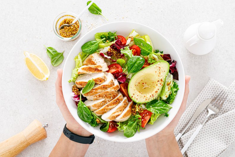 Bowl of salad topped with chicken, avocado.