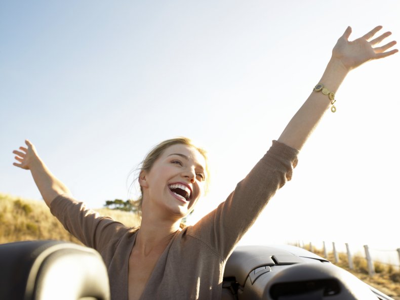 Smiling woman with hand raised in car.