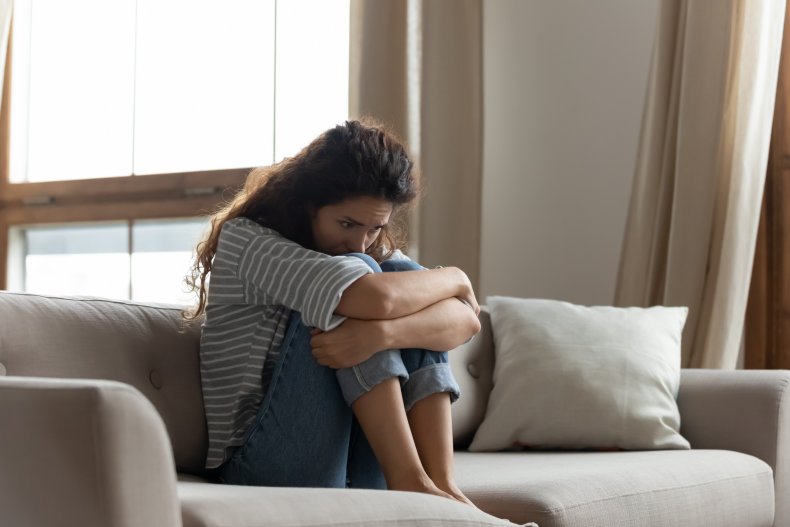 Anxious woman on sofa holding knees up.