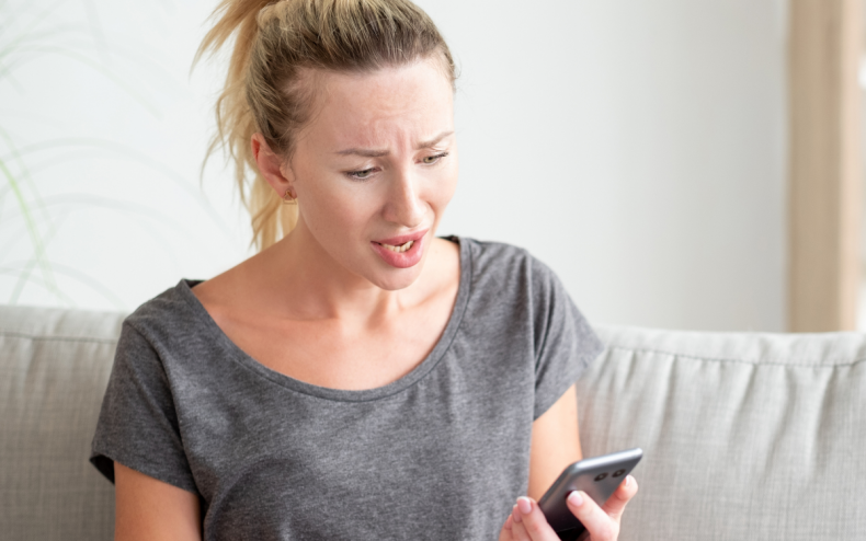 A woman looking unhappy at her phone.