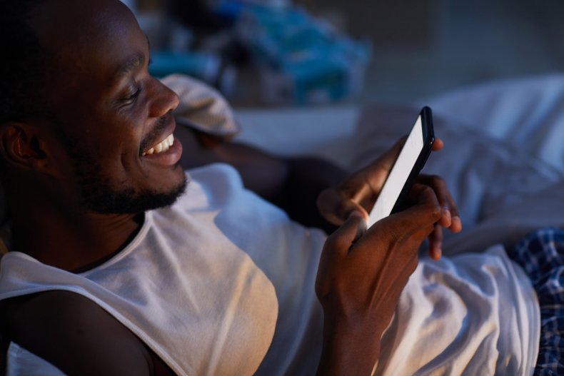 A man looking at phone in bed.