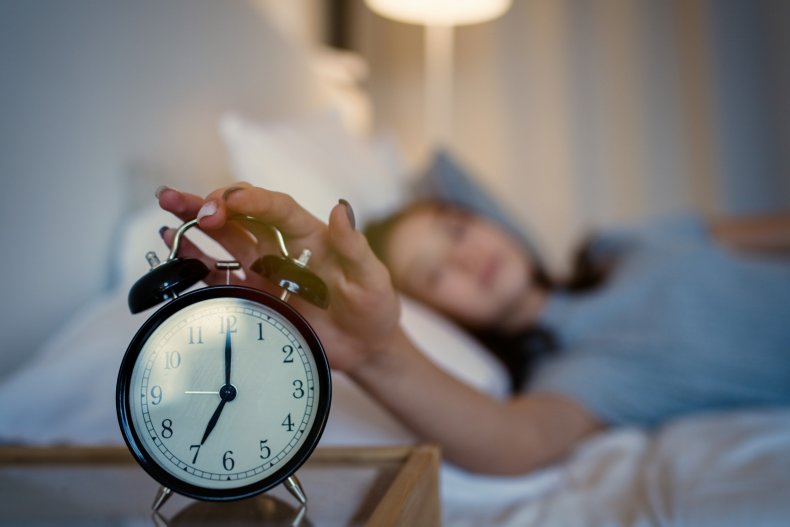 A woman with hand on bedside clock.