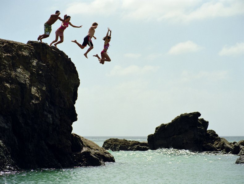 Friends jumping into ocean from rock cliff