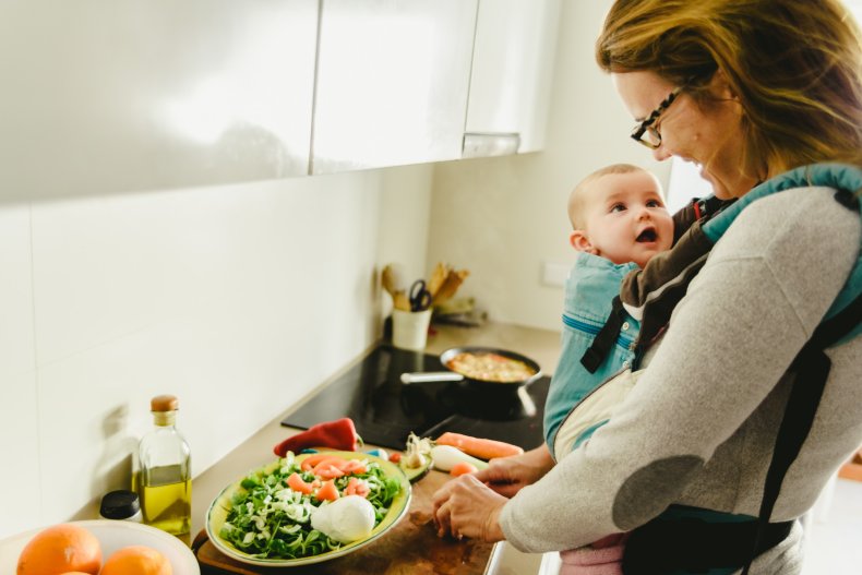 A mother cooking with baby on chest.