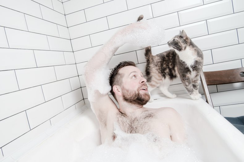 A man sitting in bath with cat.