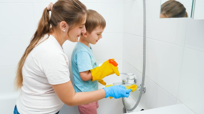 A woman cleaning bathtub with a boy.