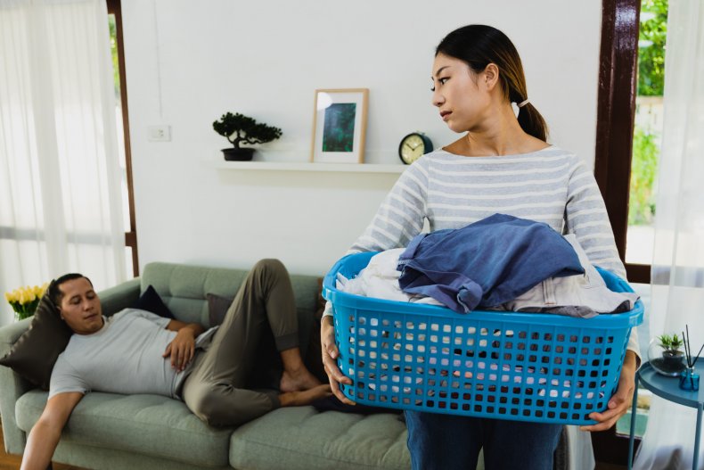 Frustrated woman doing laundry, husband sleeping.