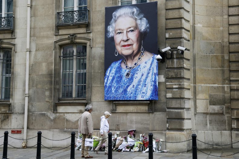 Pedestrians walk past a portrait of Queen 