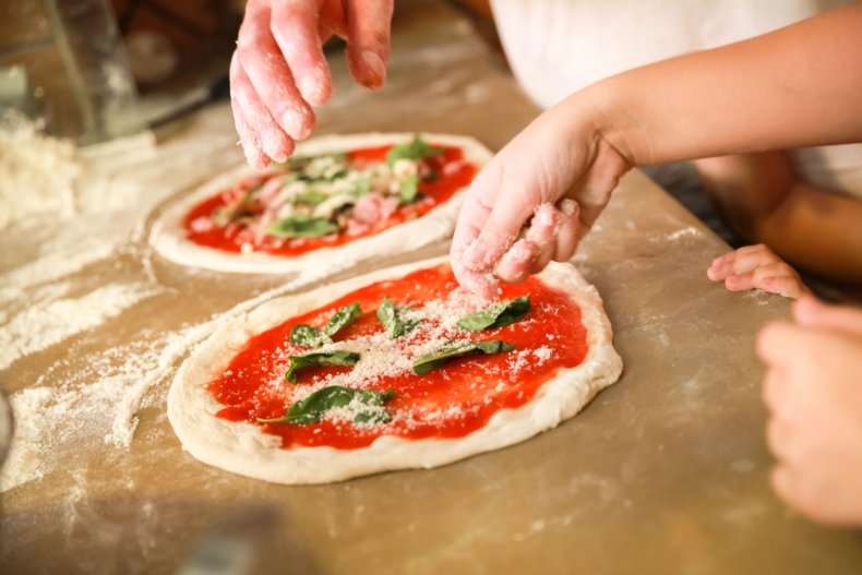Pizza being assembled with toppings on table.