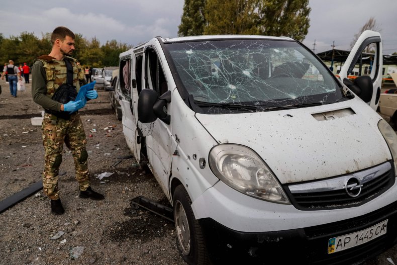 A Ukrainian soldier stands next to a badly damaged van