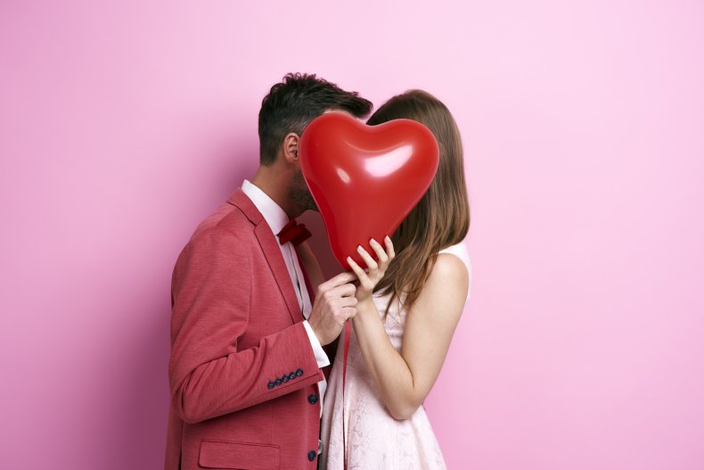 Couple kissing behind a balloon.