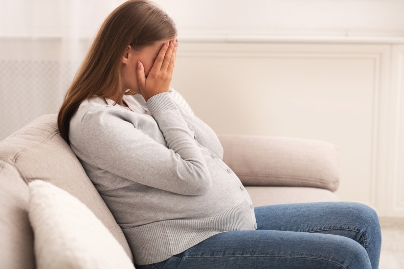 A pregnant woman crying on a sofa
