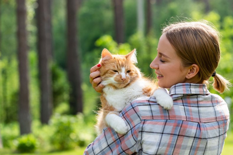 Woman cuddling a ginger cat in woodland