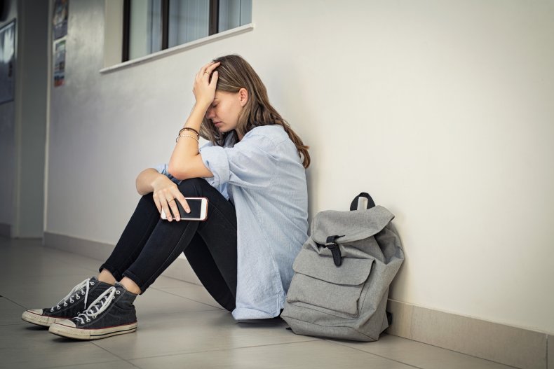 Upset teenage girl leaning against school wall