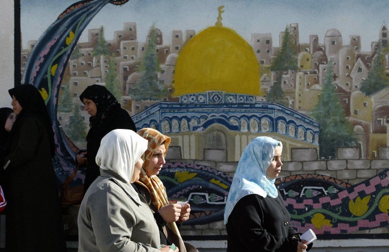 Palestinian women walk in front of mural