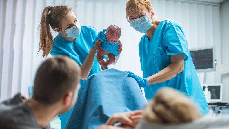 Krankenschwestern, die einem Paar ein Neugeborenes zeigen.