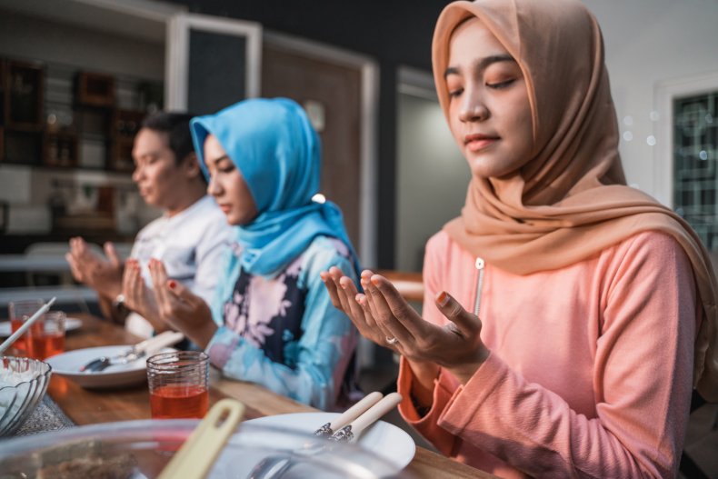 Two women wearing hijabs and man praying.