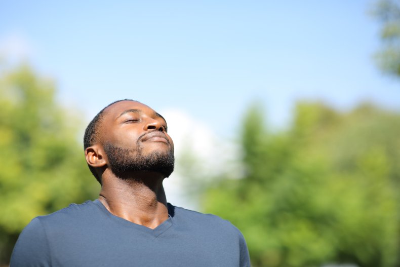 Man at park, breathing, smiling under sun.