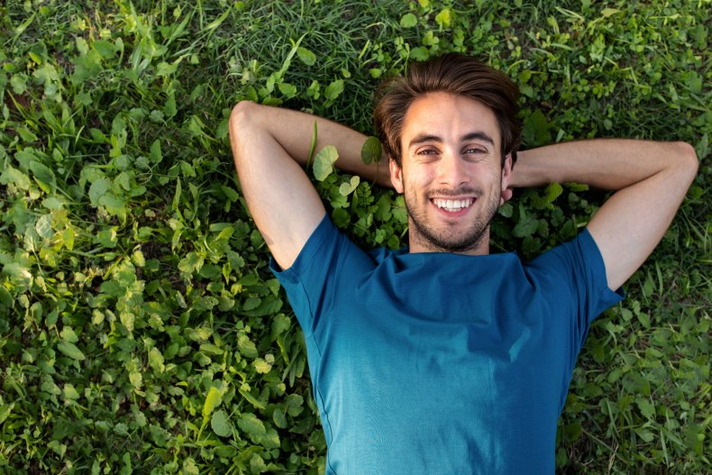 Man smiling, laying on grass at park.