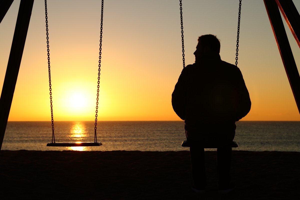 man sitting alone on swing at sunset