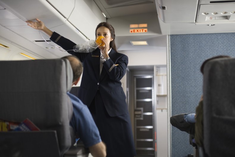 Flight attendant wearing oxygen mask on plane.