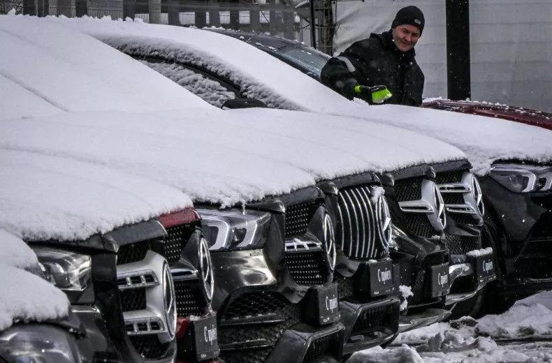 Seorang karyawan membersihkan salju dari mobil Mercedes-Benz yang diparkir di depan dealer Mercedes-Benz di Moskow, Rusia pada 14 Februari 2023. Presiden Vladimir Putin telah memerintahkan semua pejabat Rusia untuk beralih menggunakan kendaraan produksi dalam negeri.
