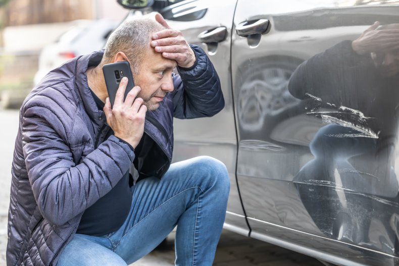 Man looking at dent in car.